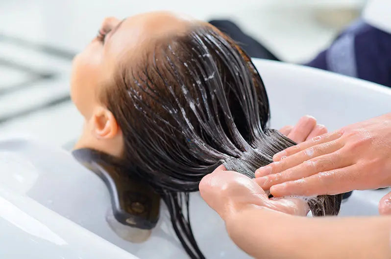 Person washing another person's hair in a sink