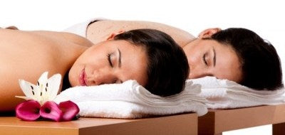 Two people receiving a massage on a spa table with white towels and flowers.