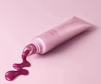 Pink cosmetic tube with purple cream spilling out on a pink background