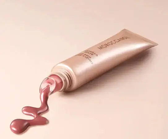 Open cosmetic tube with pink cream spilling out on a beige background
